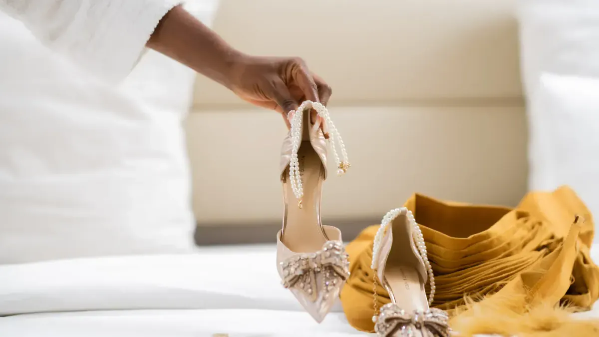 A hand holds the bride's shoes, placed next to her veil