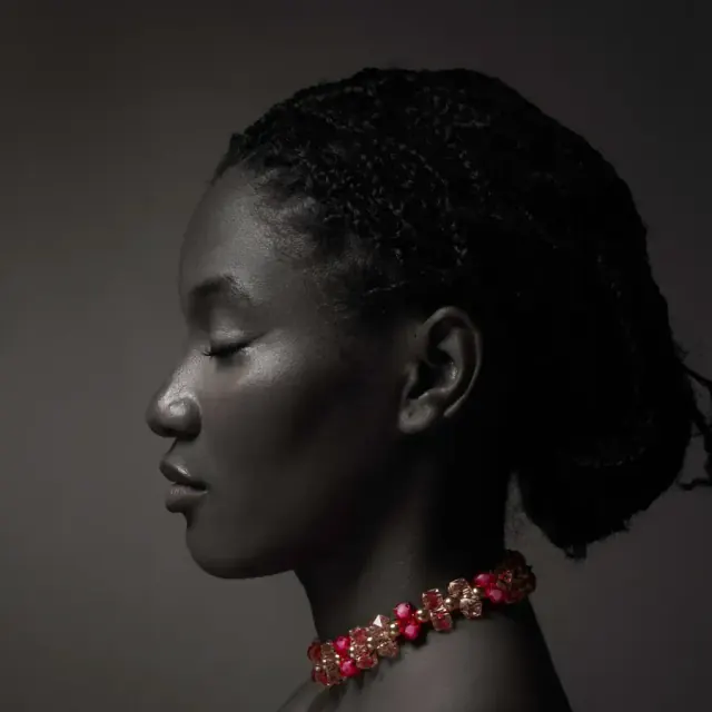 Profile portrait on a dark background, red necklace