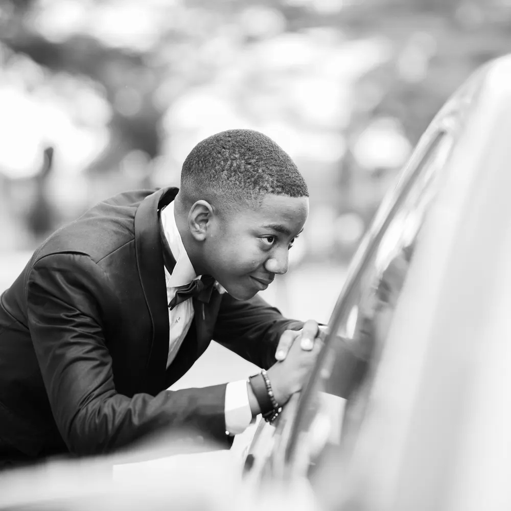 Groom in a tuxedo opening a car door, in black and white